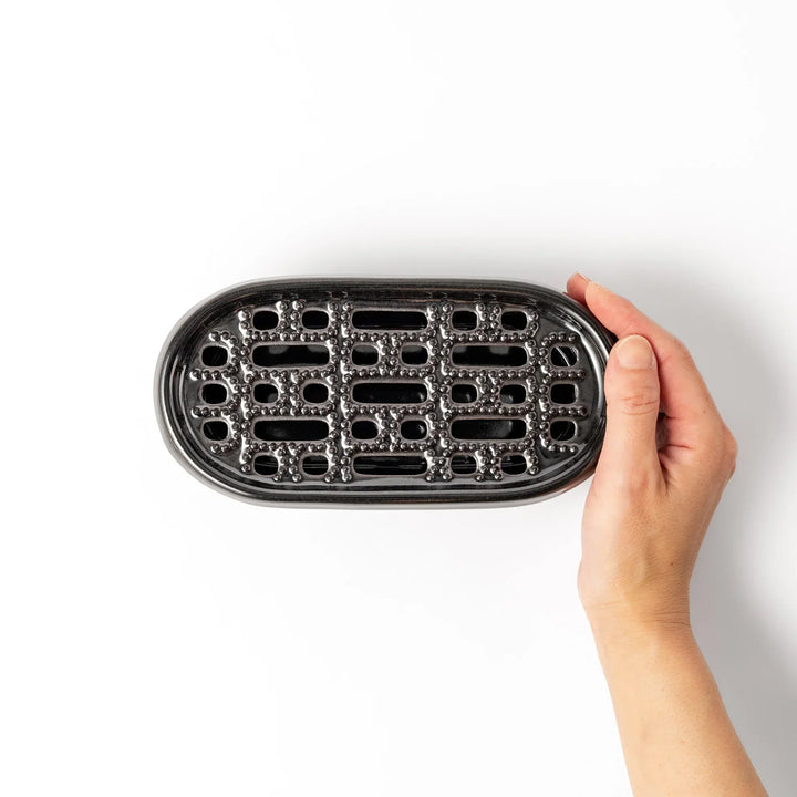 Black Japanese ceramic daikon oroshi grater with built in dish and wide holes for smooth grating cleanup.