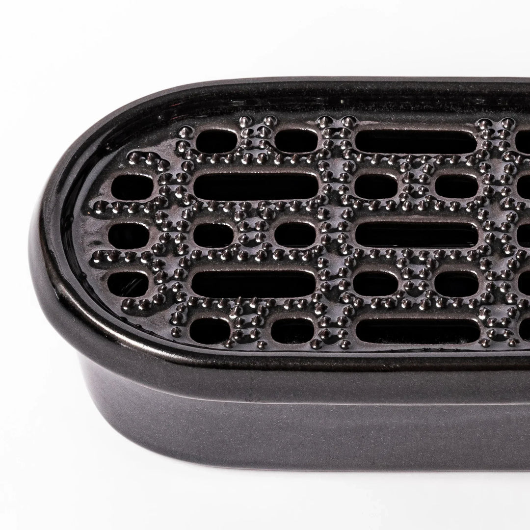 Black Japanese ceramic daikon oroshi grater with built in dish and wide holes for smooth grating cleanup.