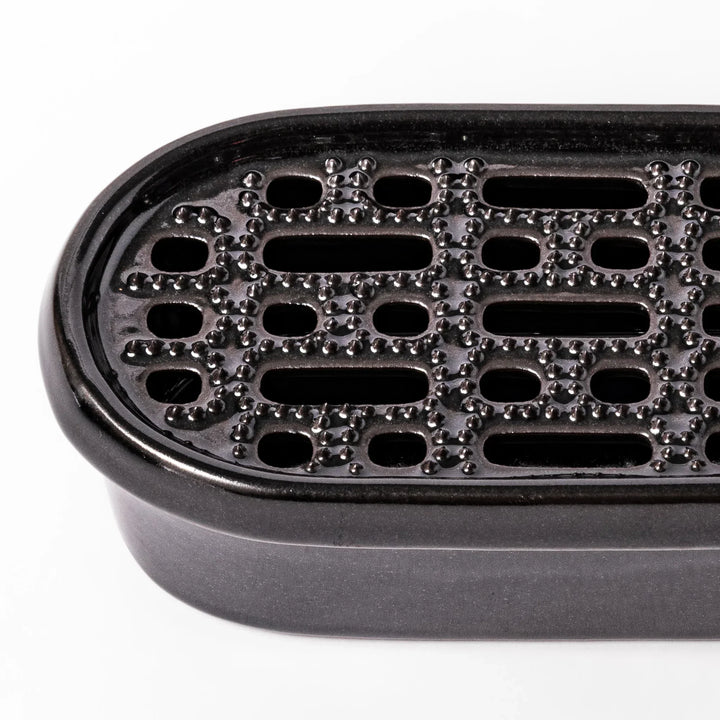 Black Japanese ceramic daikon oroshi grater with built in dish and wide holes for smooth grating cleanup.
