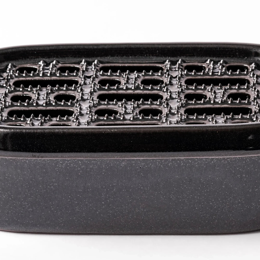 Black Japanese ceramic daikon oroshi grater with built in dish and wide holes for smooth grating cleanup.
