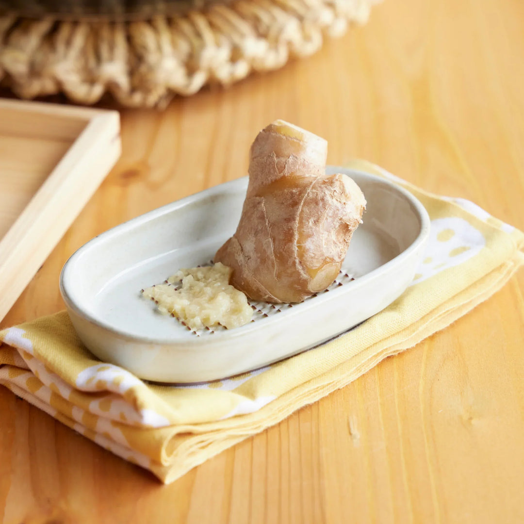 Japanese ceramic ginger grater dish with freshly grated ginger and whole root, ideal kitchen tool for authentic cooking.