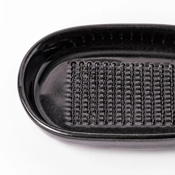 Black ceramic grater dish with raised teeth and shallow oval base, perfect for finely grating ginger, garlic, or daikon.
