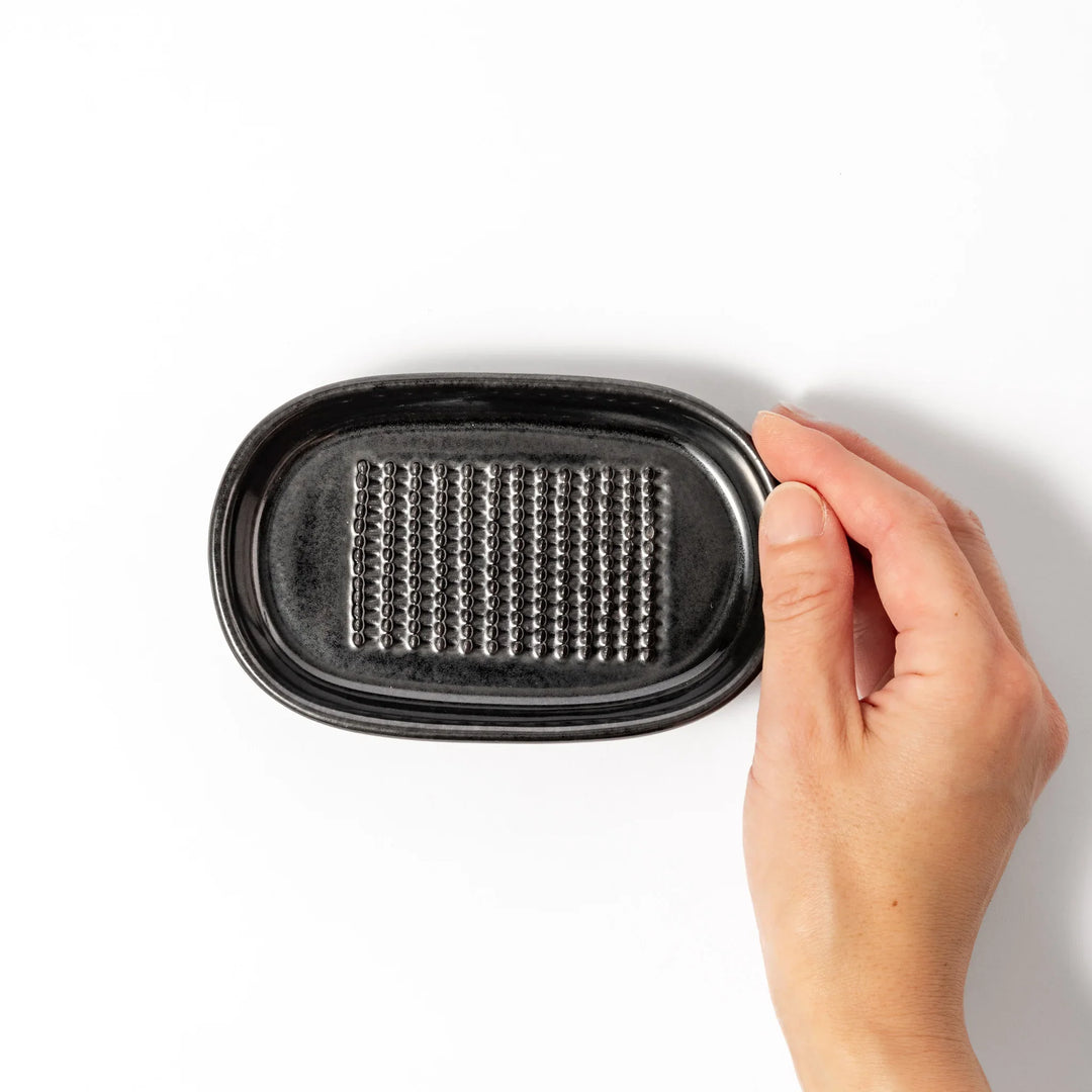 Black ceramic grater dish with raised teeth and shallow oval base, perfect for finely grating ginger, garlic, or daikon.