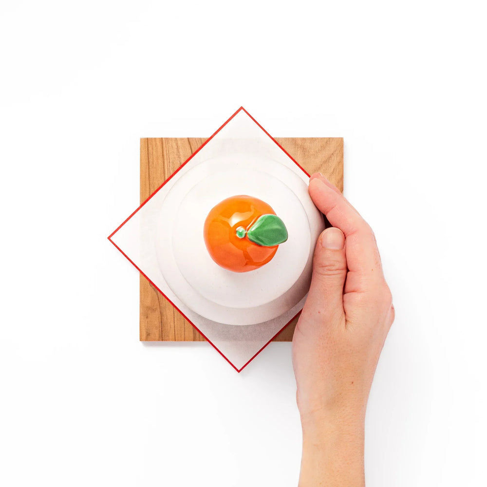 Ceramic kagami mochi jar with orange ornament on top, white two-tier design, and wooden tray for New Year decoration
