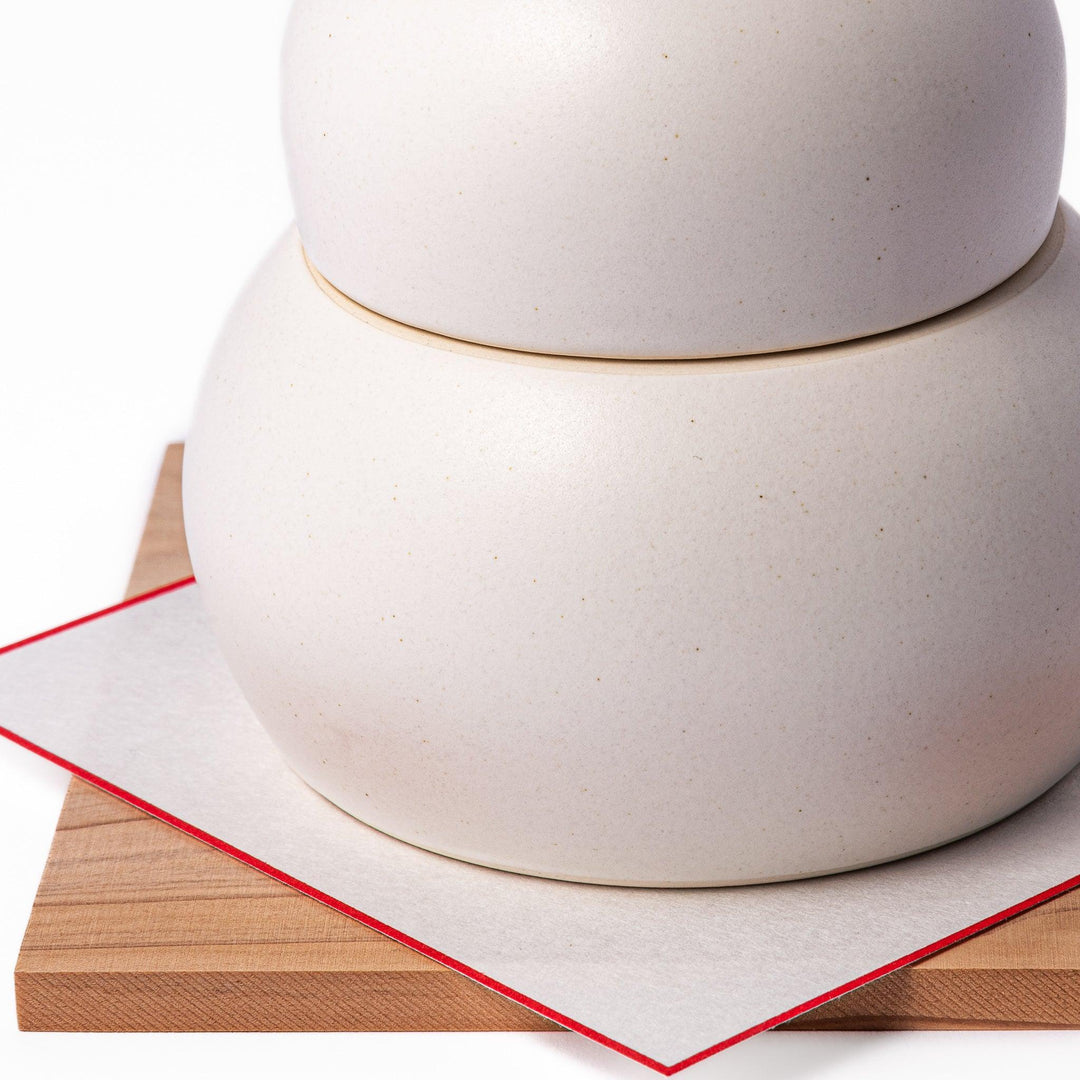Ceramic kagami mochi jar with orange ornament on top, white two-tier design, and wooden tray for New Year decoration
