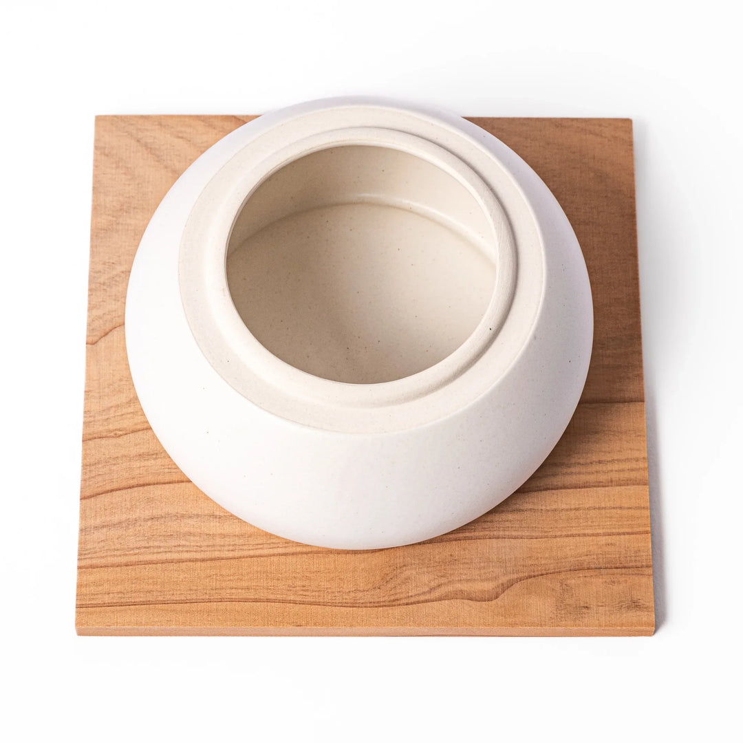 Ceramic kagami mochi jar with orange ornament on top, white two-tier design, and wooden tray for New Year decoration