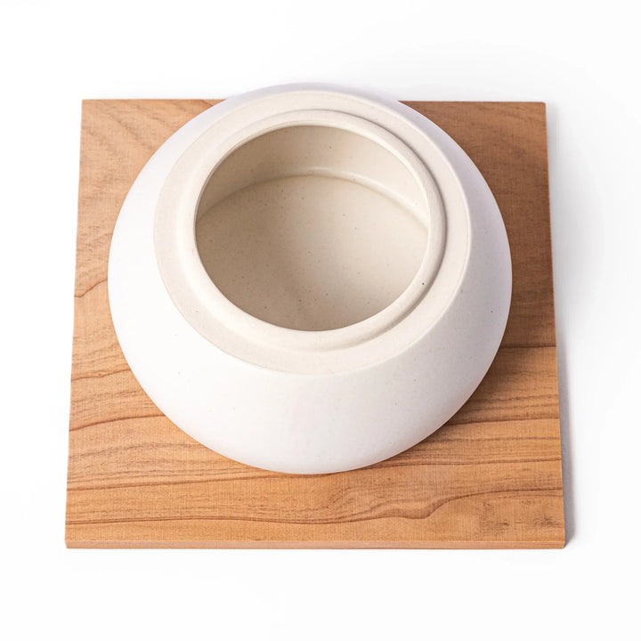 Ceramic kagami mochi jar with orange ornament on top, white two-tier design, and wooden tray for New Year decoration