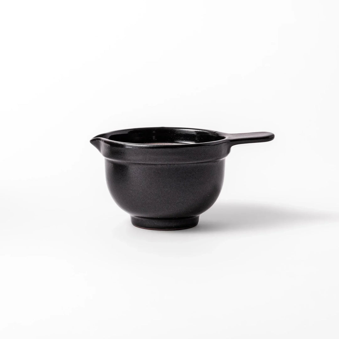 Black Japanese ceramic natto suribachi bowl with ridged brown interior and handle for mixing or grinding.