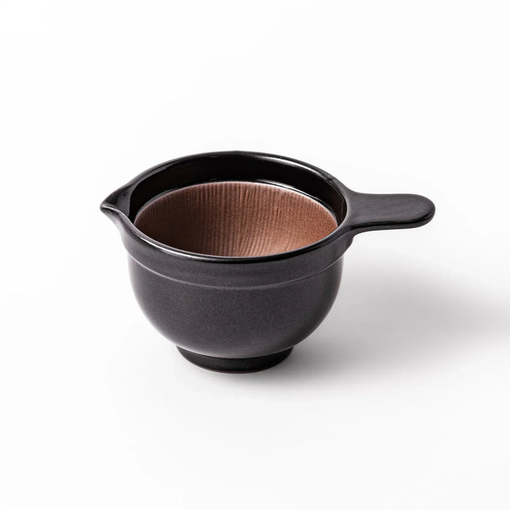 Black Japanese ceramic natto suribachi bowl with ridged brown interior and handle for mixing or grinding.