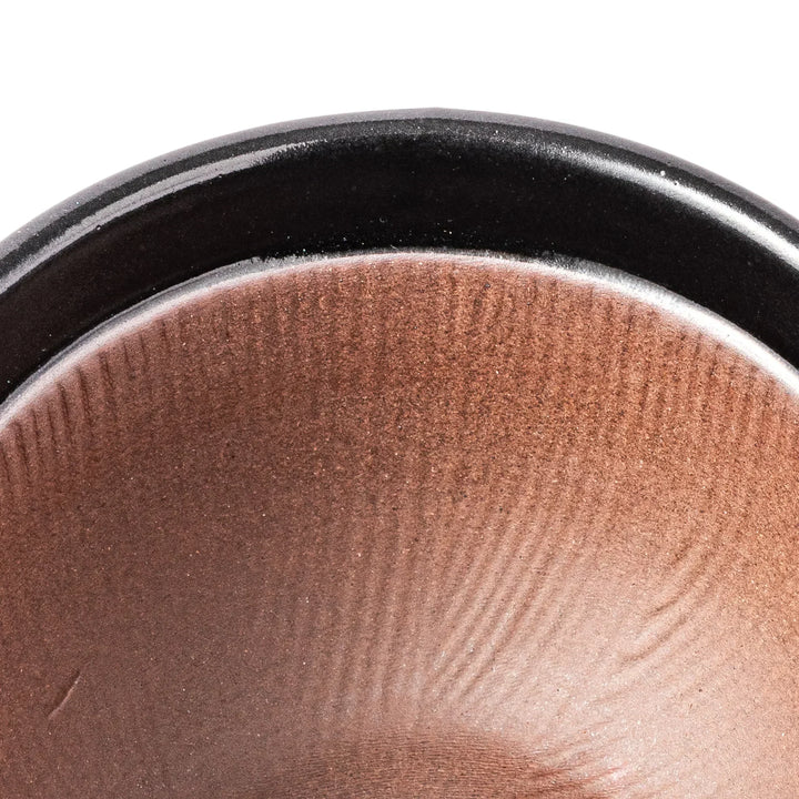 Black Japanese ceramic natto suribachi bowl with ridged brown interior and handle for mixing or grinding.