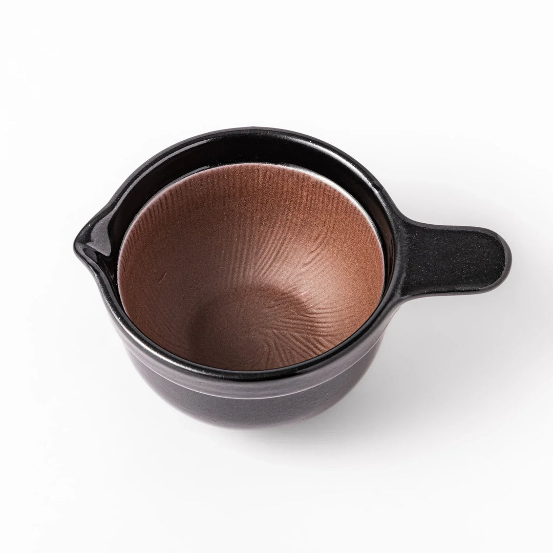 Black Japanese ceramic natto suribachi bowl with ridged brown interior and handle for mixing or grinding.