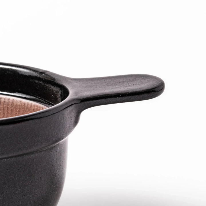 Black Japanese ceramic natto suribachi bowl with ridged brown interior and handle for mixing or grinding.