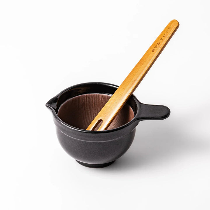 Black Japanese ceramic natto suribachi bowl with ridged brown interior and handle for mixing or grinding.