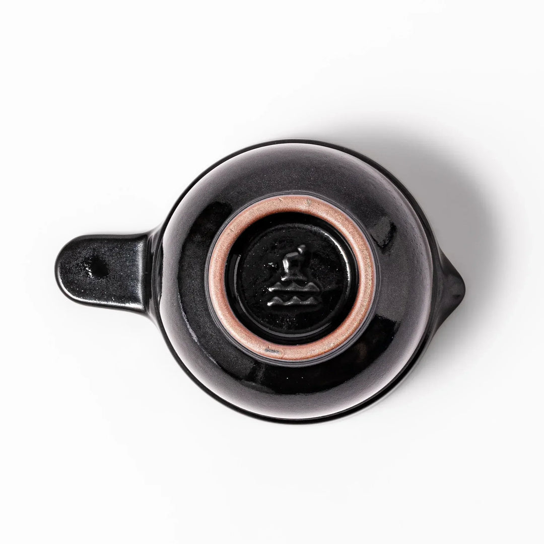 Black Japanese ceramic natto suribachi bowl with ridged brown interior and handle for mixing or grinding.