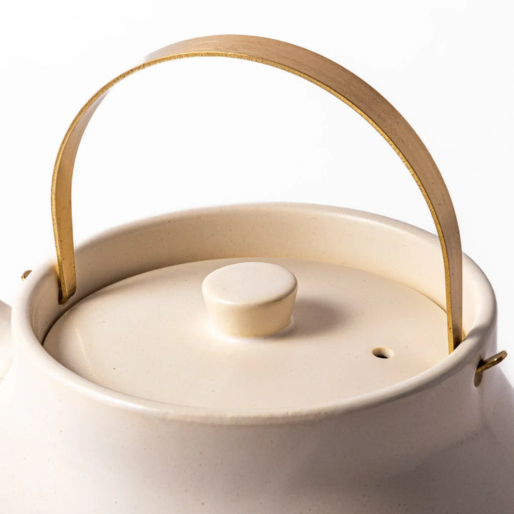 White Japanese ceramic stovetop kettle with matte finish and brass handle for daily tea brewing elegance.