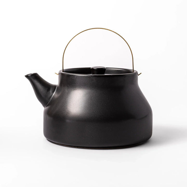 Black Japanese ceramic stovetop kettle with curved shape and brass handle for elegant functional tea time.