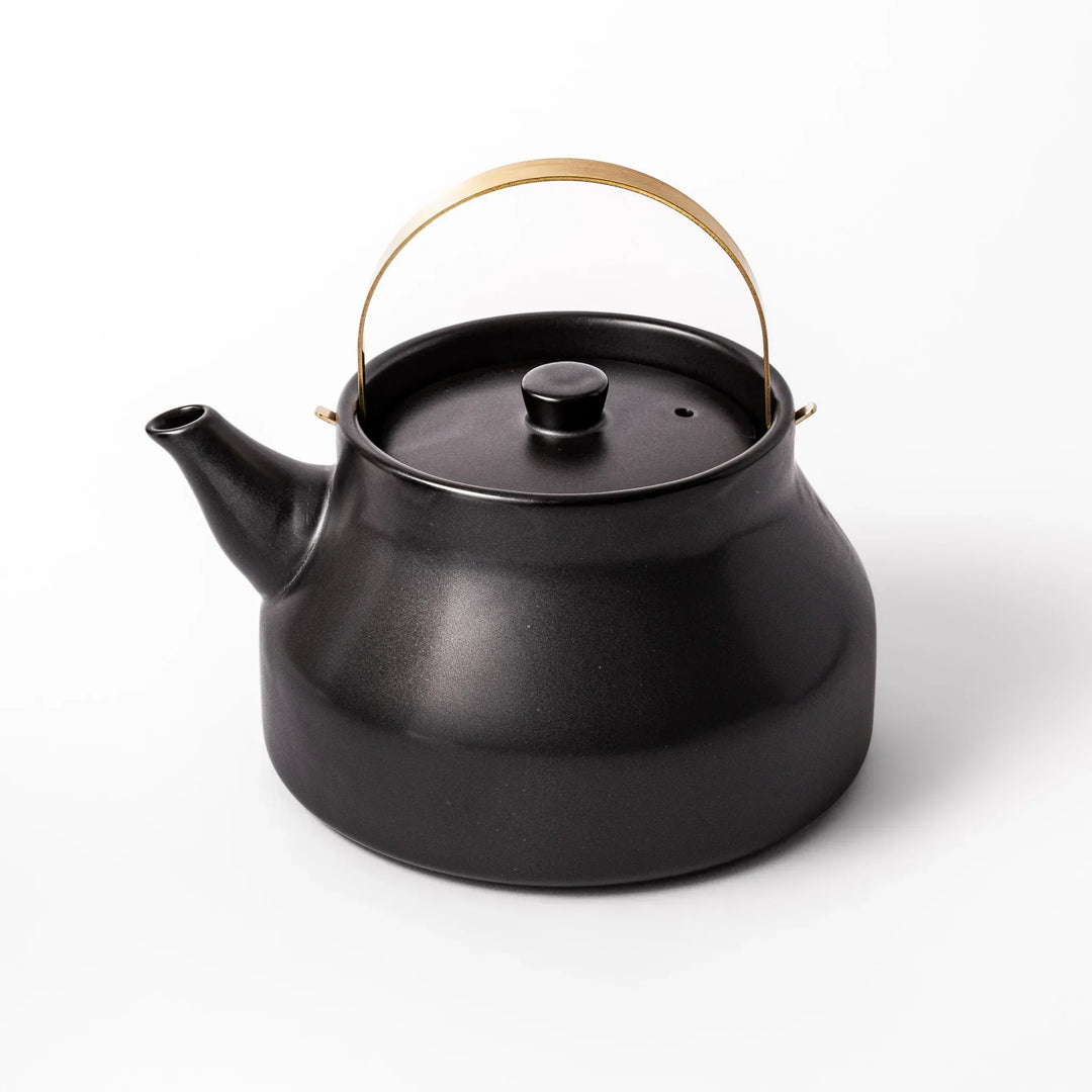 Black Japanese ceramic stovetop kettle with curved shape and brass handle for elegant functional tea time.
