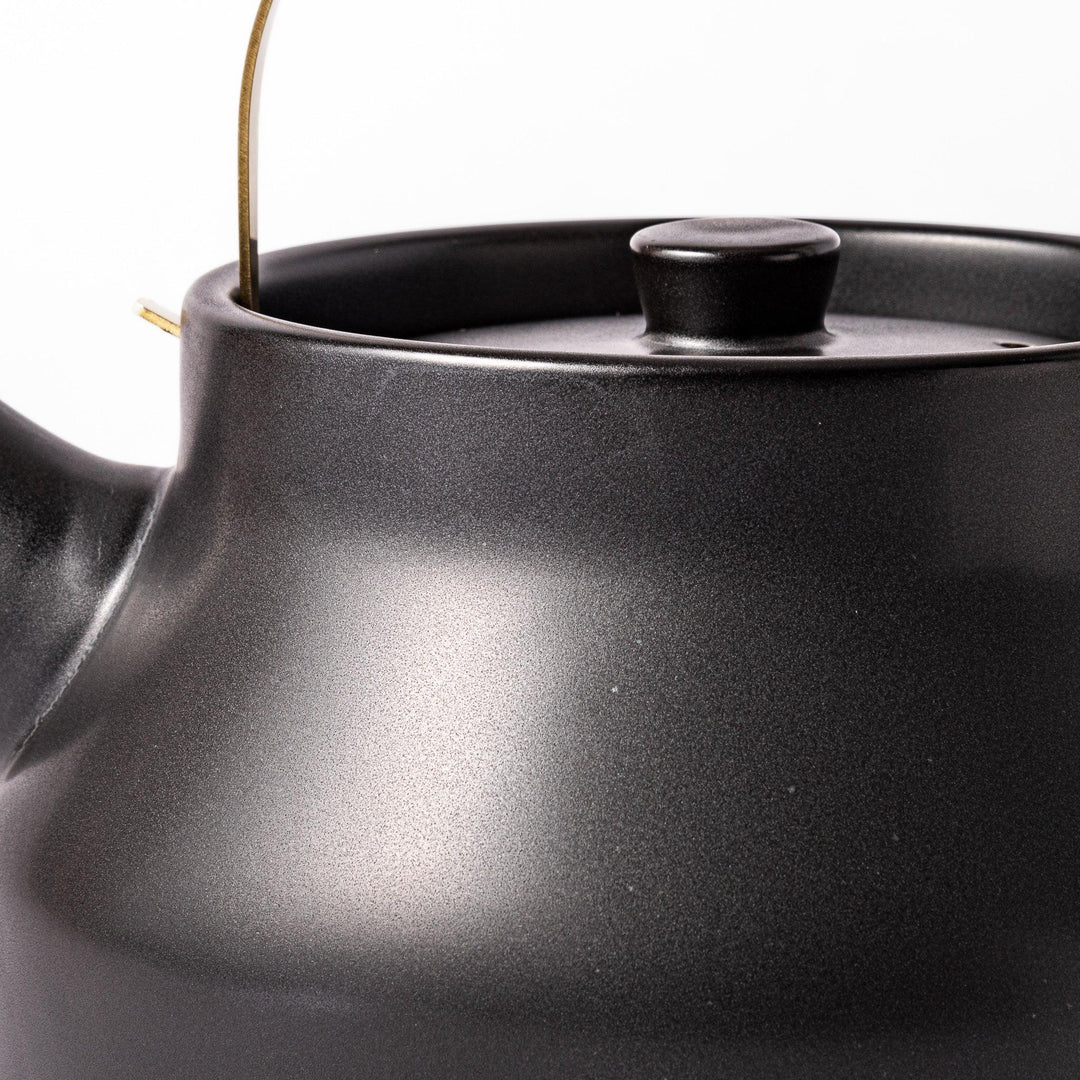 Black Japanese ceramic stovetop kettle with curved shape and brass handle for elegant functional tea time.