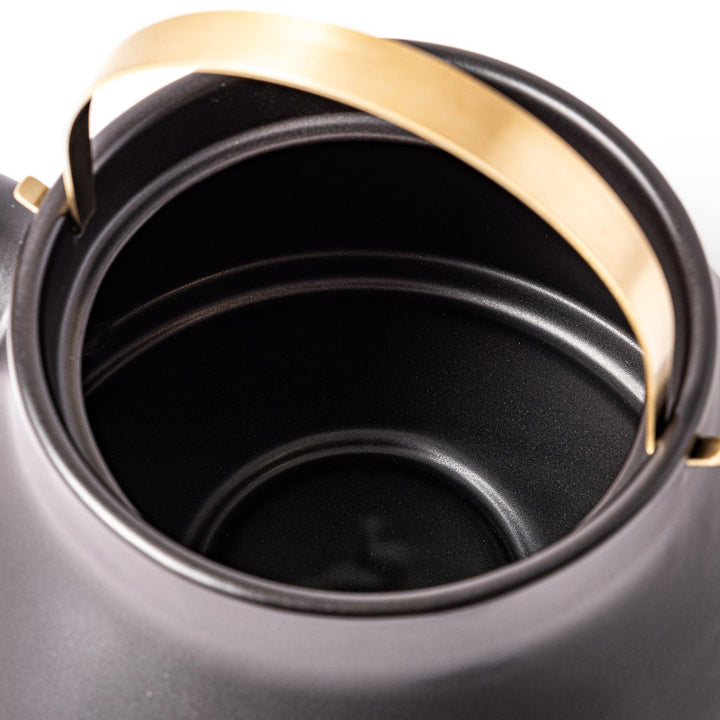Black Japanese ceramic stovetop kettle with curved shape and brass handle for elegant functional tea time.