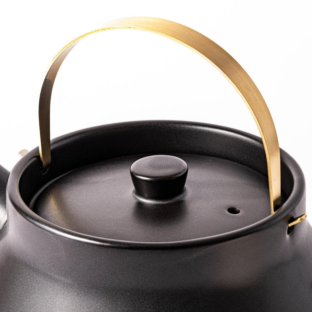 Black Japanese ceramic stovetop kettle with curved shape and brass handle for elegant functional tea time.