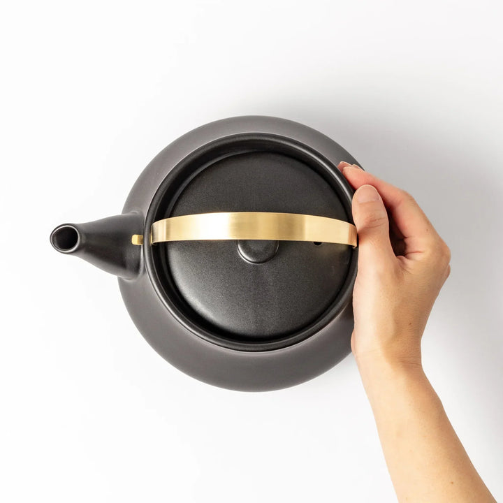 Black Japanese ceramic stovetop kettle with curved shape and brass handle for elegant functional tea time.