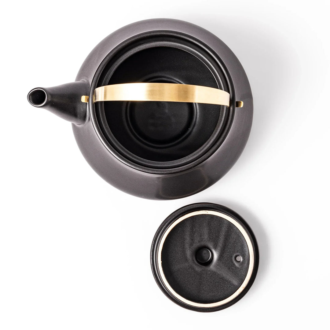 Black Japanese ceramic stovetop kettle with curved shape and brass handle for elegant functional tea time.