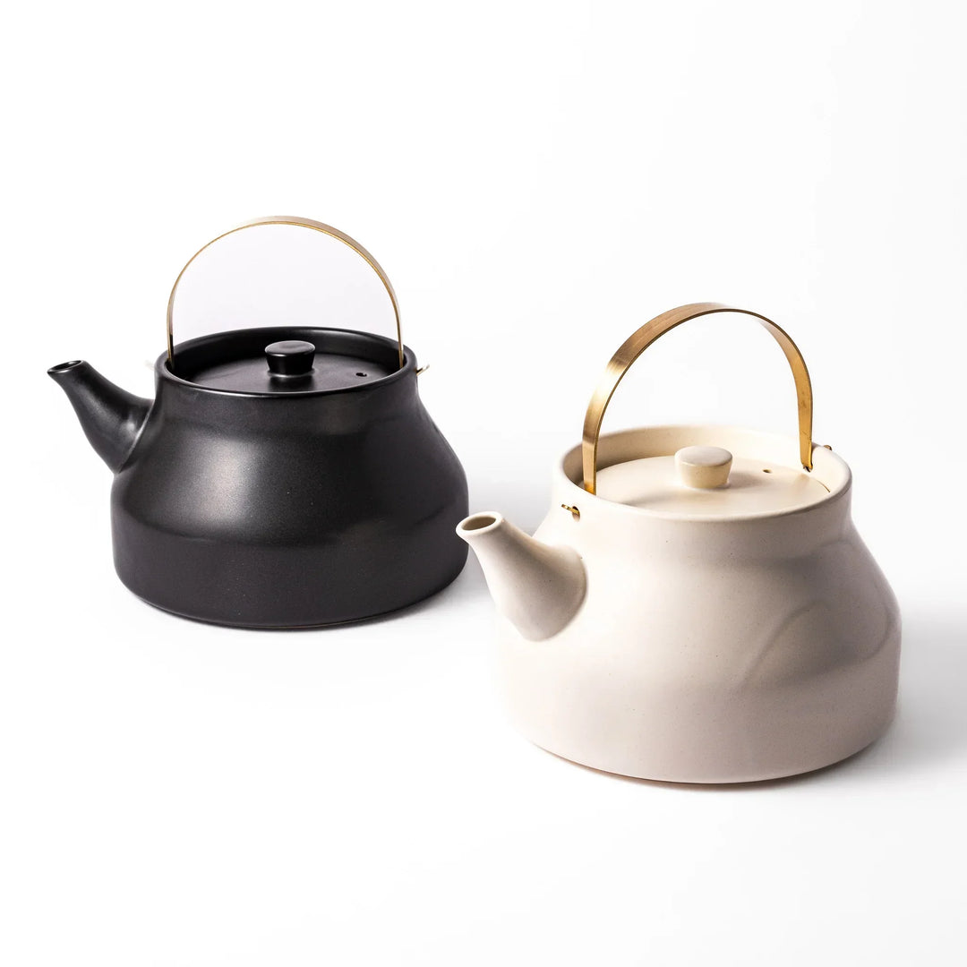Japanese ceramic stovetop kettles in black and white with brass handles for modern elegant tea preparation.