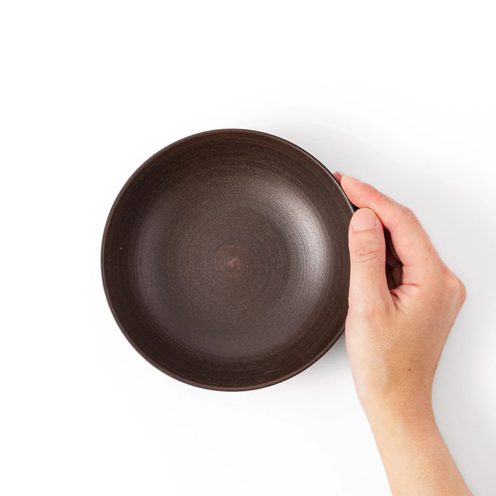 Matte brown ceramic bowl with a gently curved form and subtle textured finish, placed on a white background.