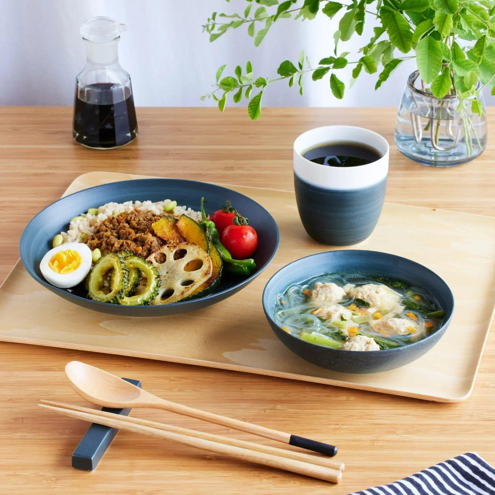 Navy blue dinnerware set with rice dish, soup bowl, and cup, paired with wooden chopsticks and spoon on a wooden tray.