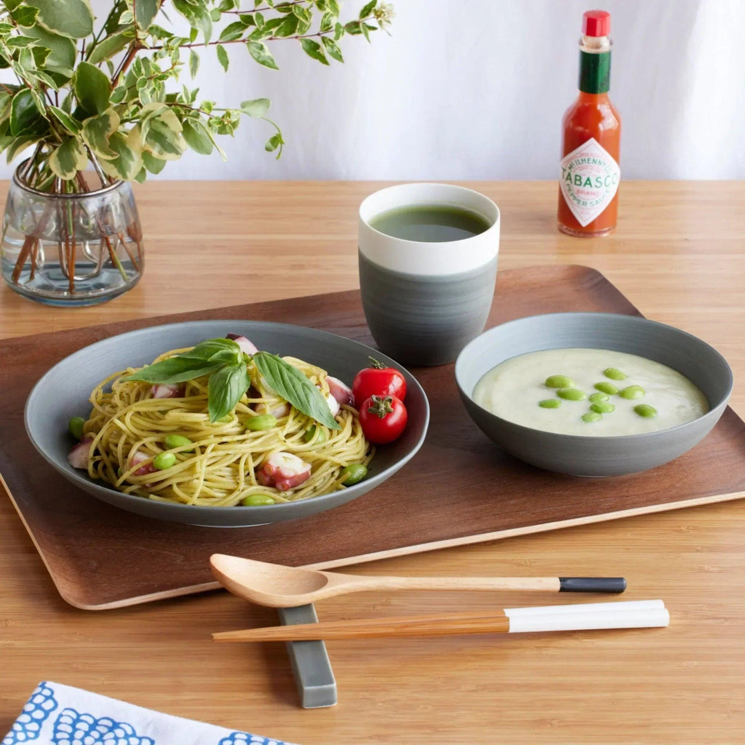 Cozy Japandi 4-Piece Dinnerware Set in gray, featuring a tea cup, pasta plate, and soup bowl, displayed on a wooden tray with a modern meal setting.