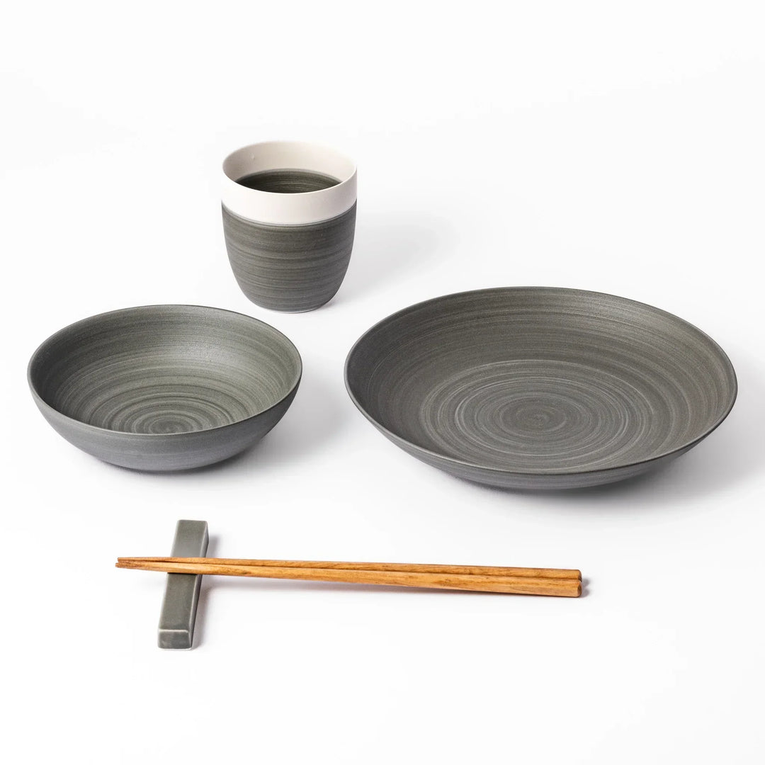 Japandi-style table setting in cool gray tones featuring a salad plate, bowl, tea cup, and chopsticks with rest.