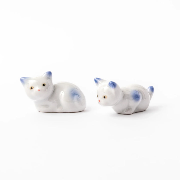 Porcelain chopstick rests shaped like playful kittens, white with soft blue accents on ears, tail, and body.