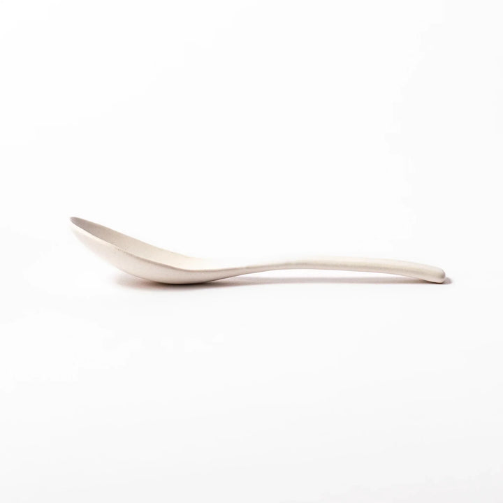 White ceramic scoop spoon with angled handle and deep, curved bowl for smooth serving of soup, stew, or curry.