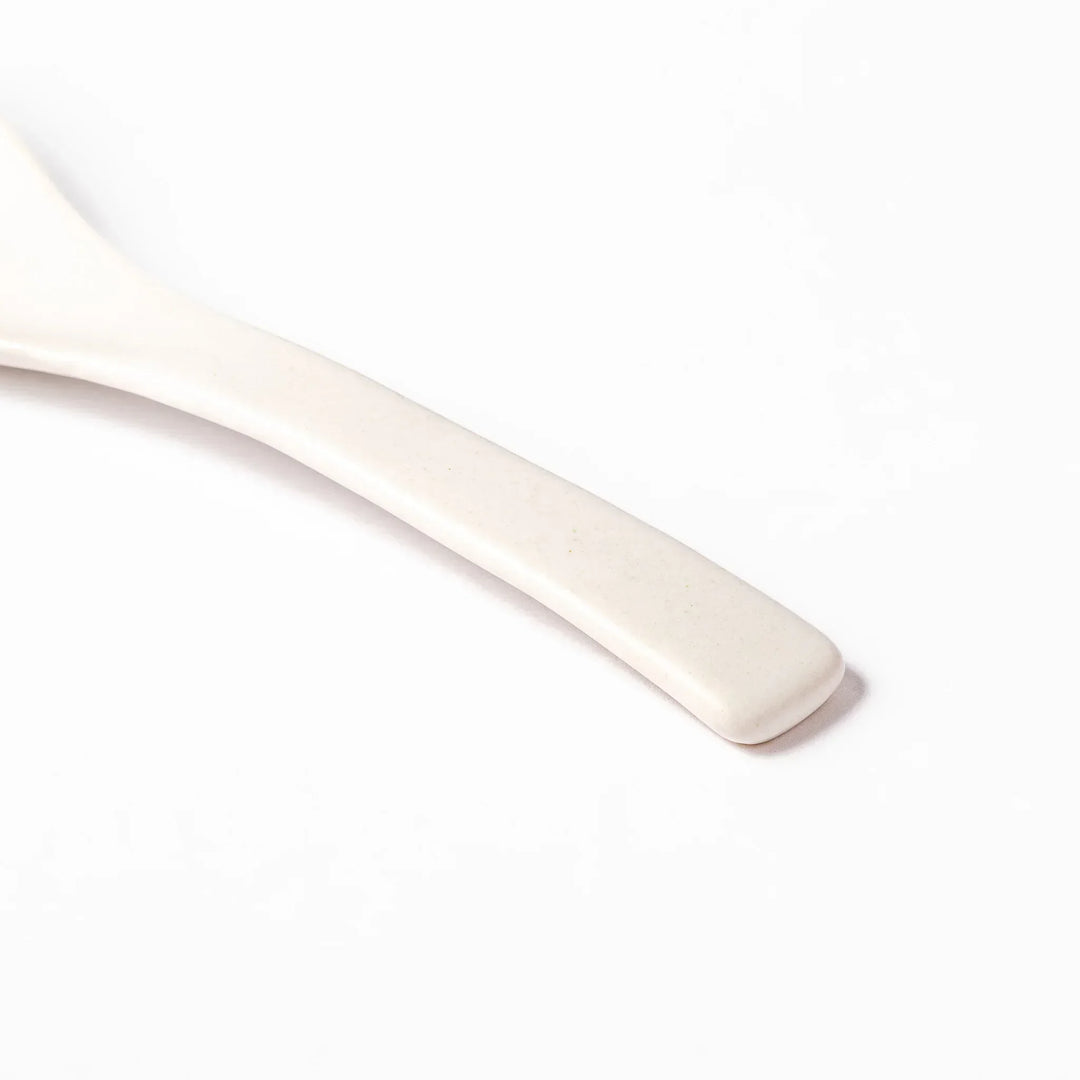 White ceramic scoop spoon with angled handle and deep, curved bowl for smooth serving of soup, stew, or curry.