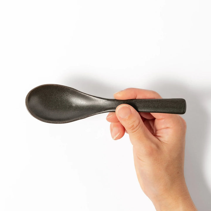 Black Japanese ceramic spoon with smooth rounded bowl and straight handle for serving soup stew or curry.