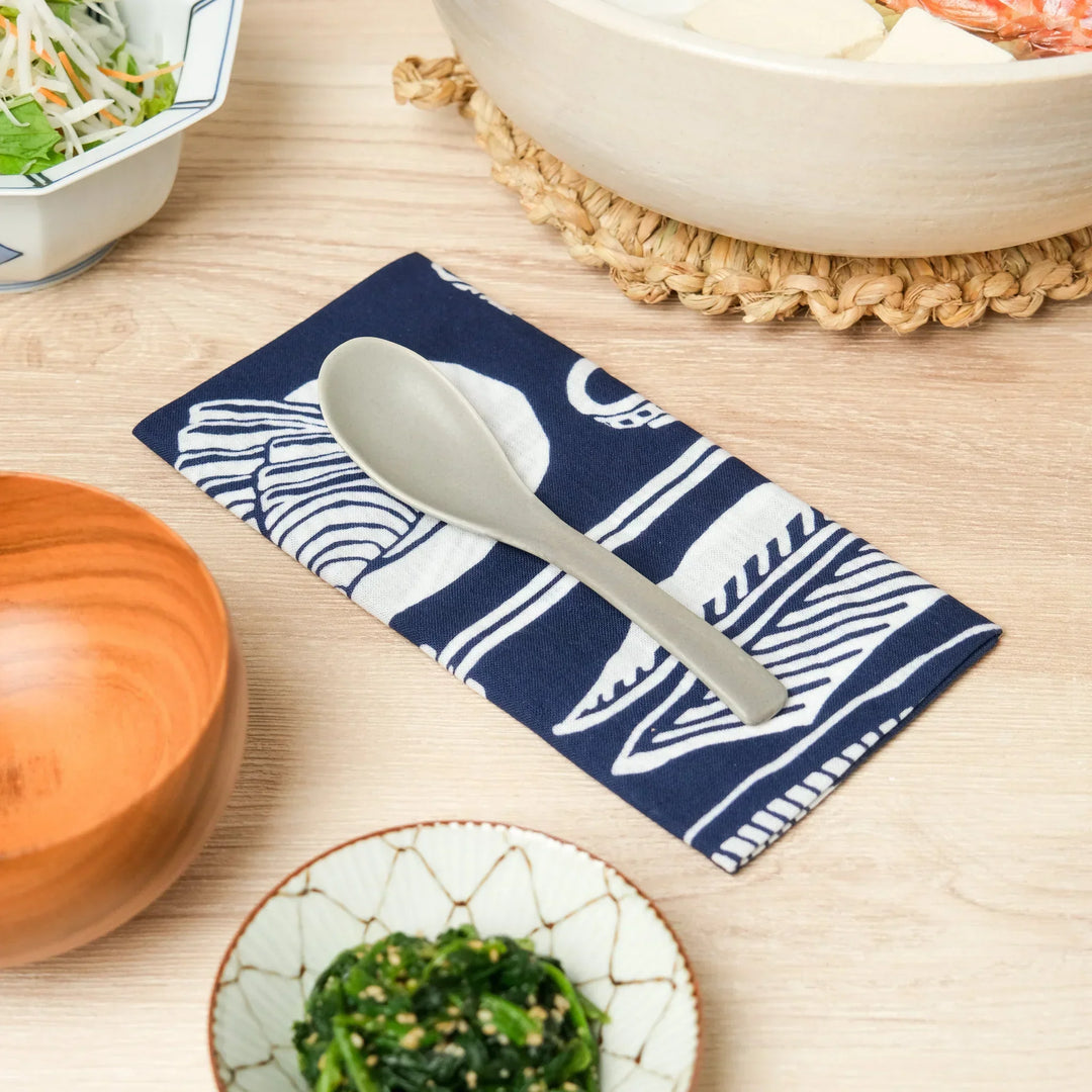 Japanese ceramic soup spoon on indigo tenugui cloth for serving donabe hot pot and traditional meals.