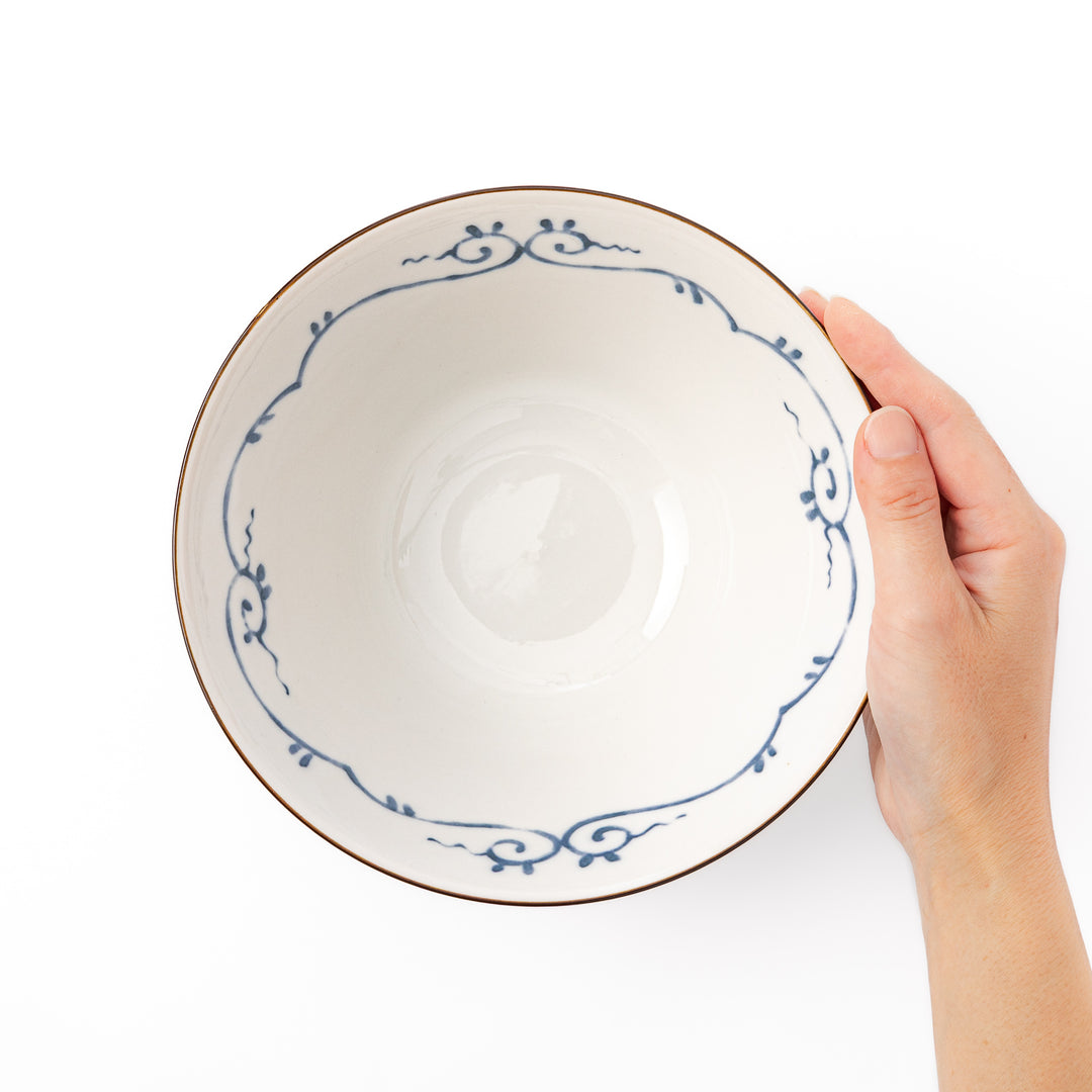A blue red and white ceramic Japanese ramen bowl featuring a cute dinosaur silhouette amidst traditional pine and floral patterns
