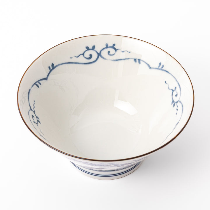 A blue red and white ceramic Japanese ramen bowl featuring a cute dinosaur silhouette amidst traditional pine and floral patterns