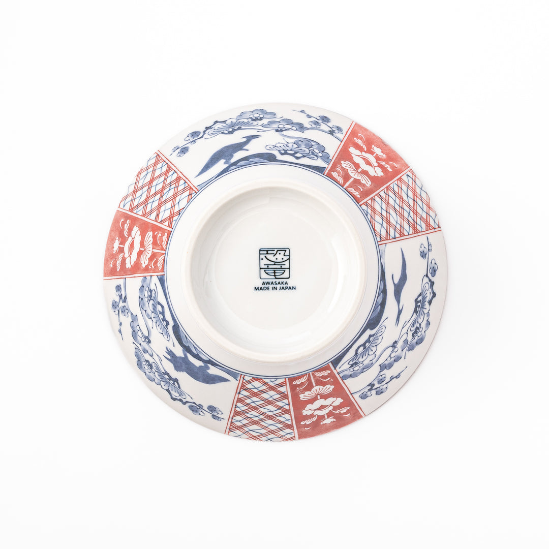 A blue red and white ceramic Japanese ramen bowl featuring a cute dinosaur silhouette amidst traditional pine and floral patterns