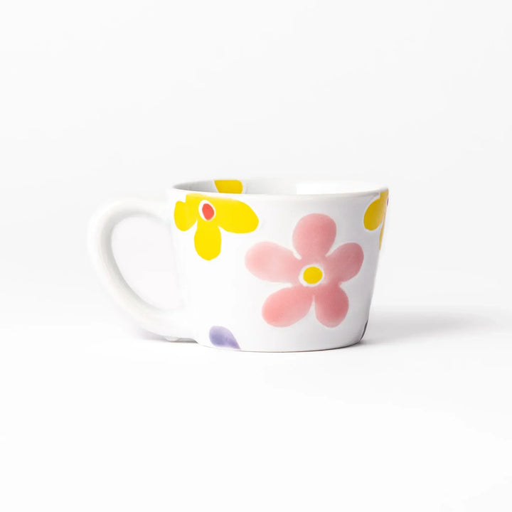 White ceramic kids mug with pink, yellow, red, and purple flower motifs, round handle, shown held for scale