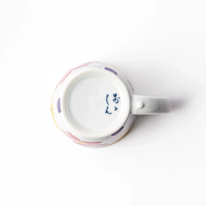 White ceramic kids mug with pink, yellow, red, and purple flower motifs, round handle, shown held for scale