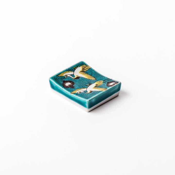 Rectangular Japanese ceramic chopstick rest with flying crane motif teal geometric background and gold accents.