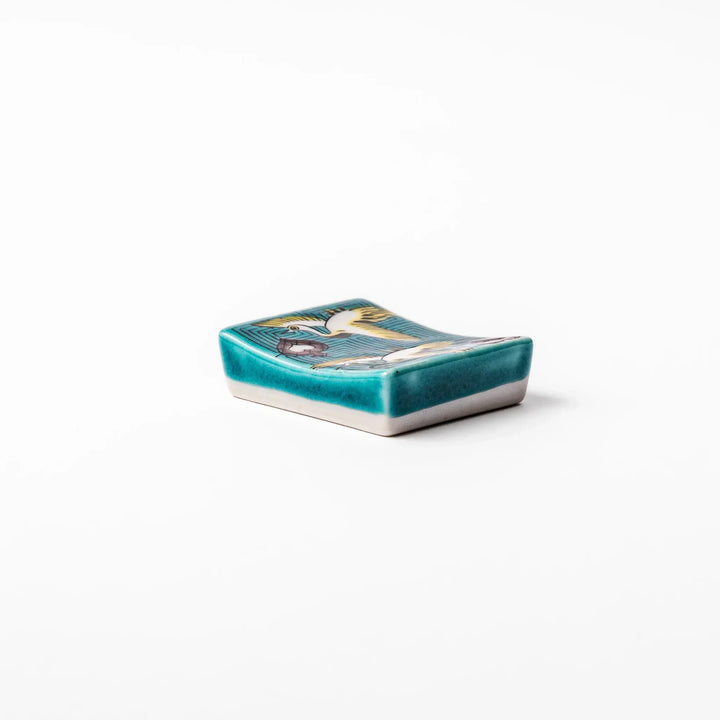 Rectangular Japanese ceramic chopstick rest with flying crane motif teal geometric background and gold accents.