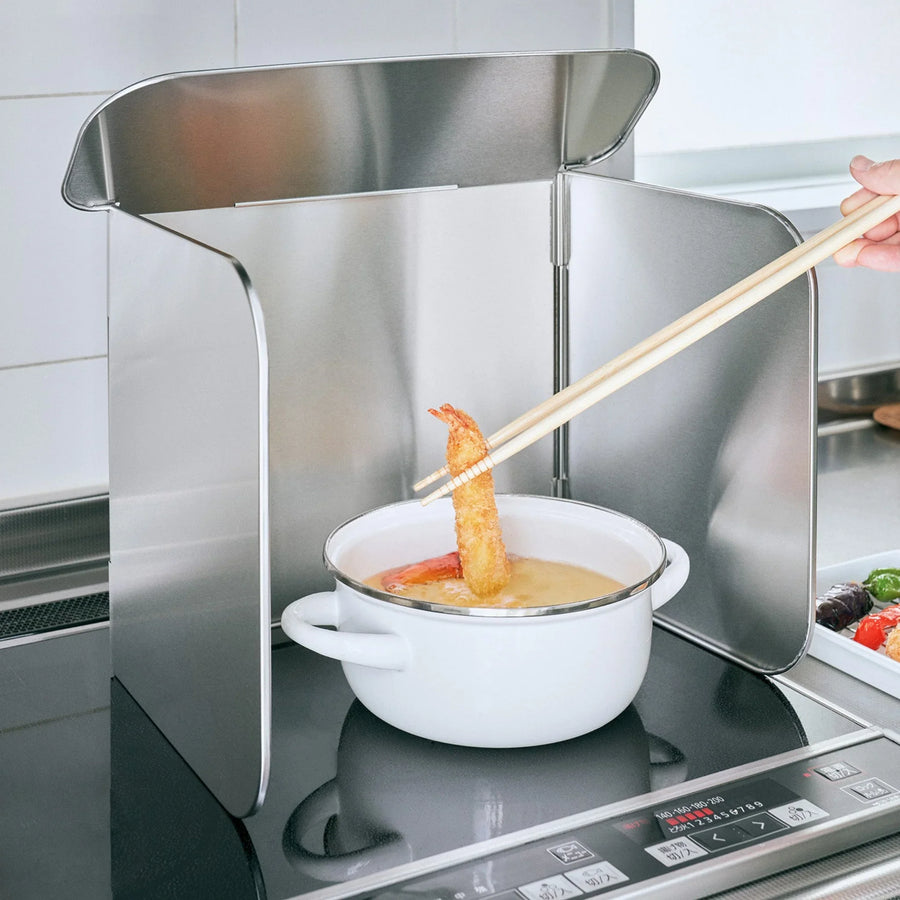 Stainless steel stove splatter guard surrounding a pot of oil while frying shrimp on an induction cooktop