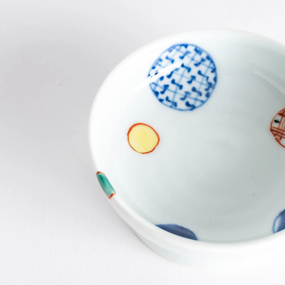 A small, round raised sauce dish featuring geometric circles in various colors, providing a textured, artistic design.