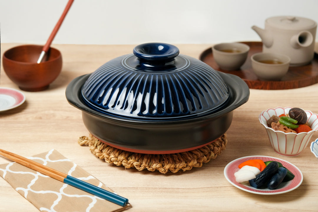 Blue ceramic Japanese donabe on a table surrounded by side dishes and tea cups