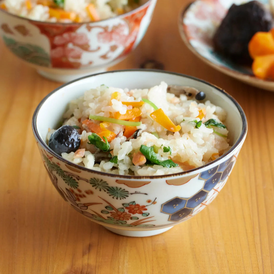 Japanese porcelain rice bowl with floral and geometric designs filled with mixed rice with carrots and greens.