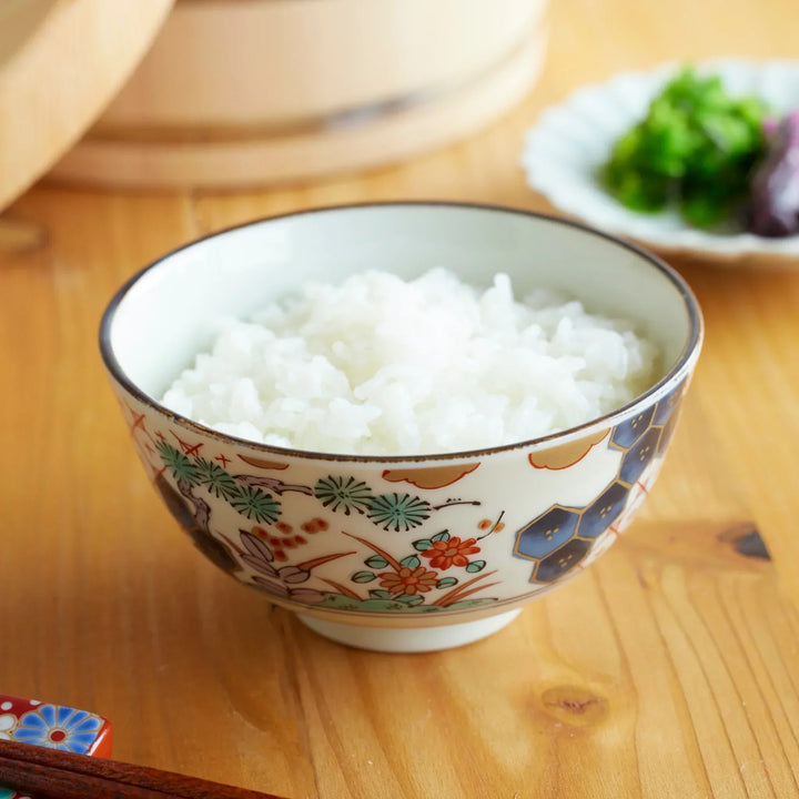 Japanese rice bowl with traditional floral and hexagon patterns, filled with freshly cooked white rice on a wooden table.