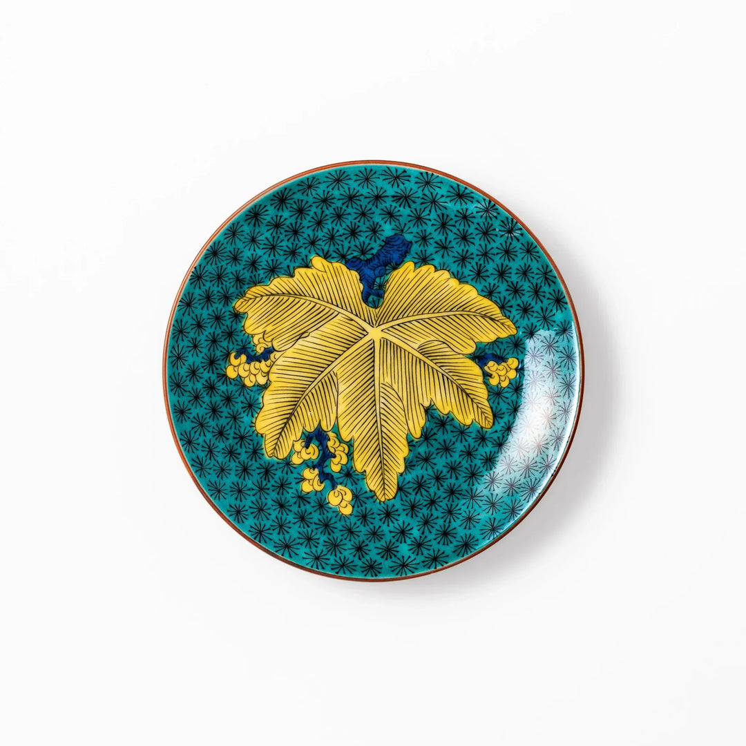 Round Kutani dessert plate with a bold golden leaf and grape motif on a turquoise background patterned with black starbursts.