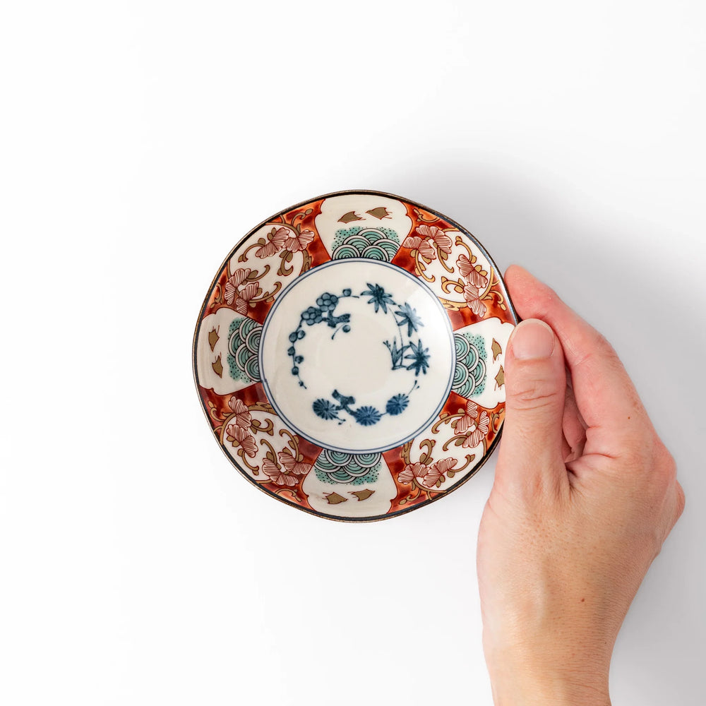 Scalloped Japanese dessert bowl with red green and gold patterns and blue floral center for elegant dining.